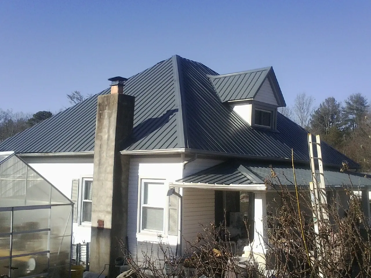 Dark blue standing seam metal roof on a white farmhouse with dormer — Slate & Tile Roof Repair by Roofing Brothers in Glen