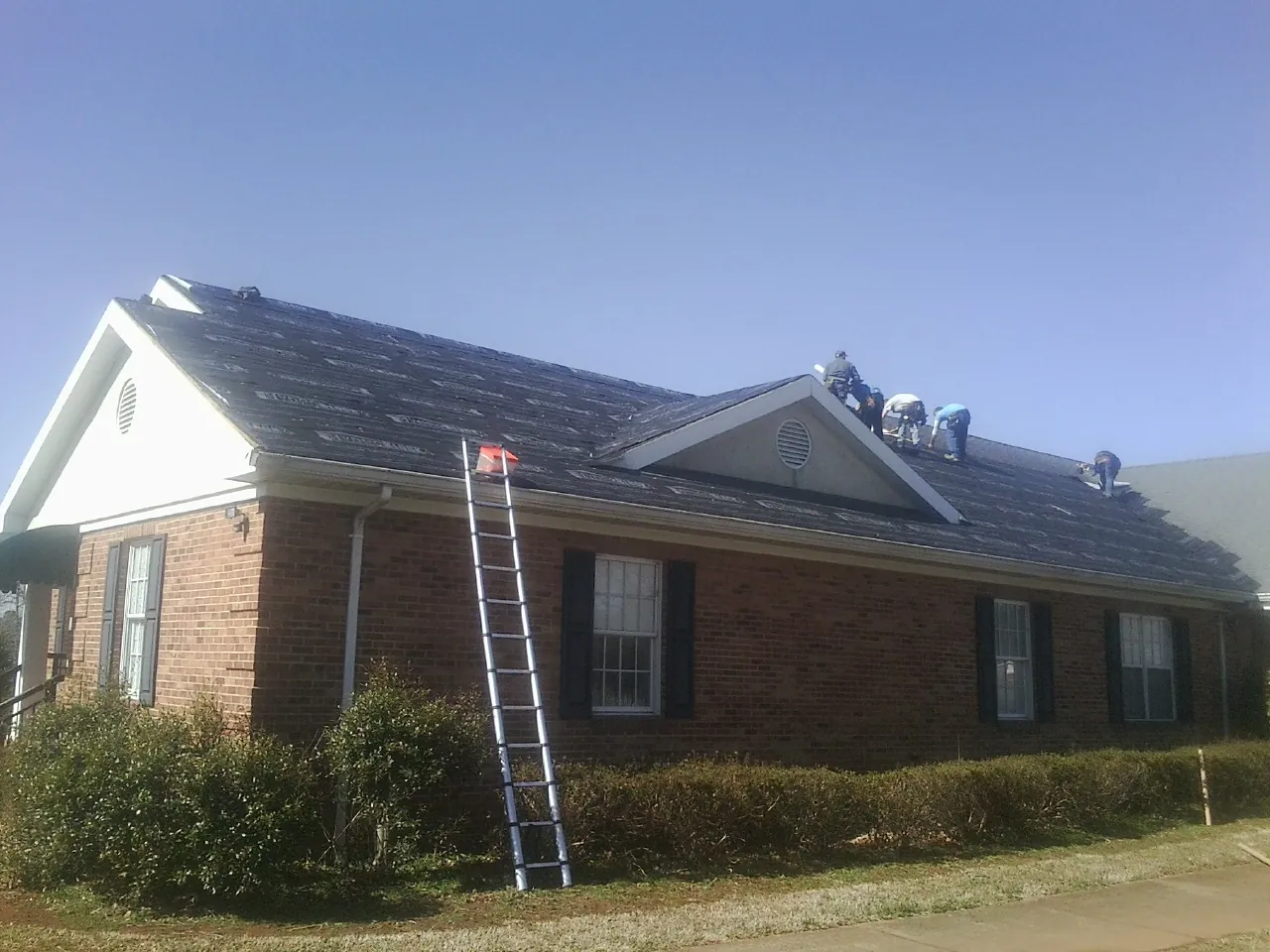 Crew tearing shingles off a brick ranch roof with a ladder set — Metal Roof Repair work by our crew in Glen