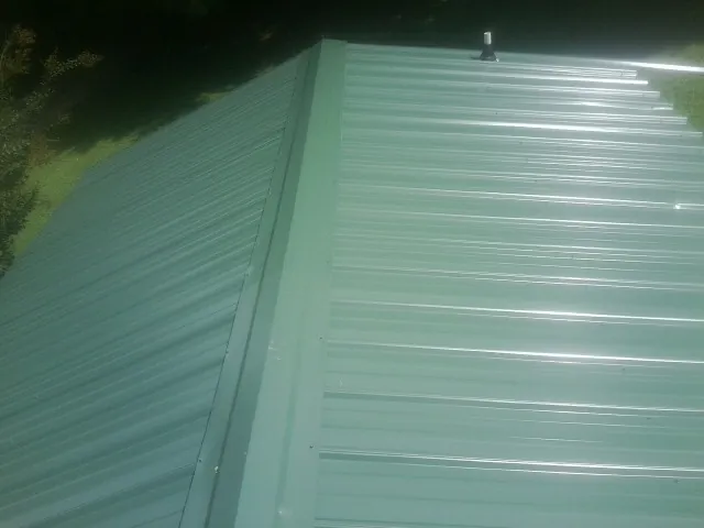 New green metal panels meeting at the ridge of a roof — Flat Roof Repair work by our crew in Glen