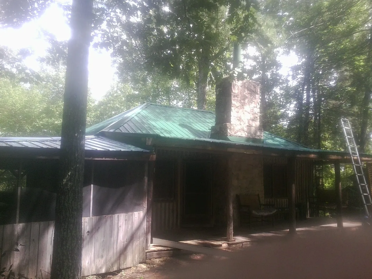 Green metal roof and stone chimney above a log cabin porch in Glen