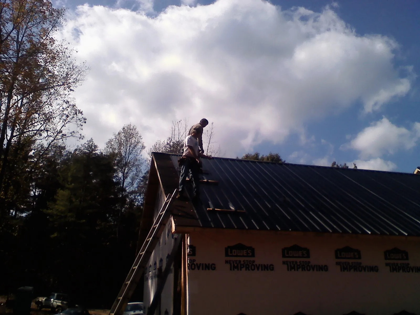Roofer fastening dark metal panels high against a cloudy sky, from a Roof Inspection job in Glen