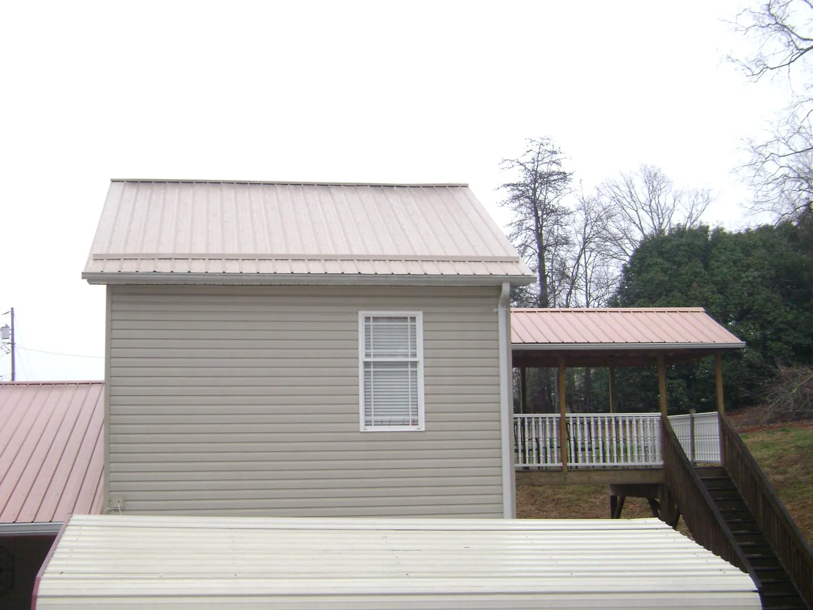 Tan metal roofs on a two story addition and attached porch, from a Roof Replacement job in Glen